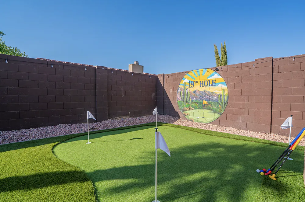 A putting green on artificial turf with three flags, against a painted desert wall.
