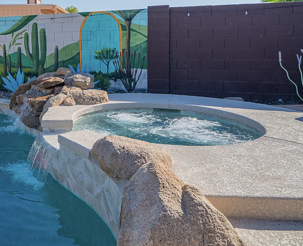 A swimming pool with a rock waterfall running into it and a hot tub set beside it.