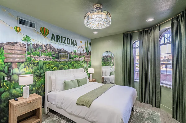 A bedroom with one bed against a painted mural of Arizona landmarks and hot air balloons.