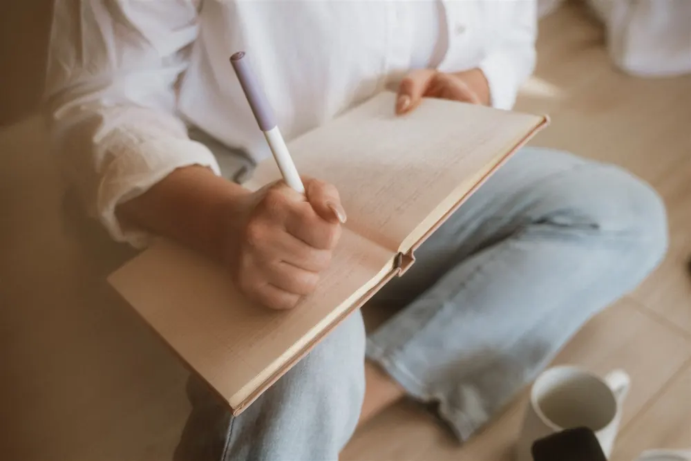 Close-up of Cydnie writing in a linen-bound journal with a lavender pen