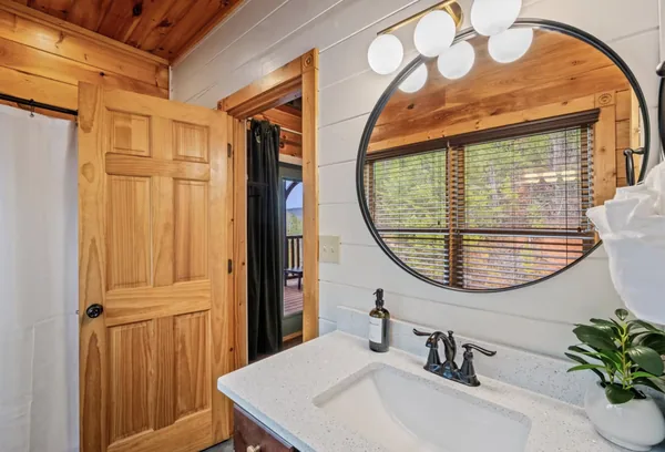 A bathroom with a round mirror over a stone counter and a window onto the trees.