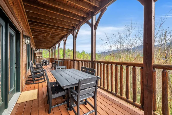 A covered deck with a long table and rocking chairs, looking across to a mountain ridge.
