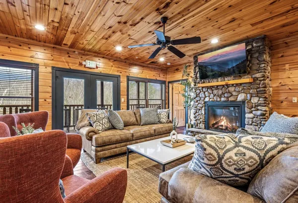 The great room, sofas and armchairs around a stone fireplace under a timber ceiling.