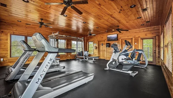 A gym under a pine ceiling with treadmills and a cable machine on black matting.