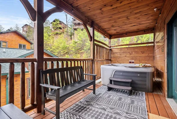 A hot tub on a covered deck with a bench beside it and the treeline beyond the rail.