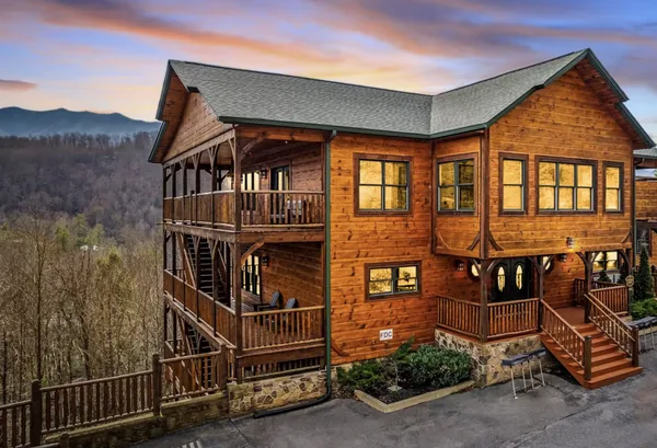 The house on its wooded slope at dusk, windows lit, the ridgeline behind it.