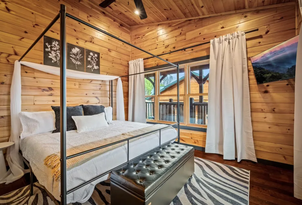 A four poster king bed with white linen, facing glass doors onto a private balcony with the mountains beyond.