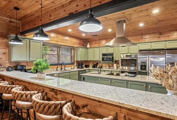 The kitchen from the counter, pendant lights over a long island with stools along it.
