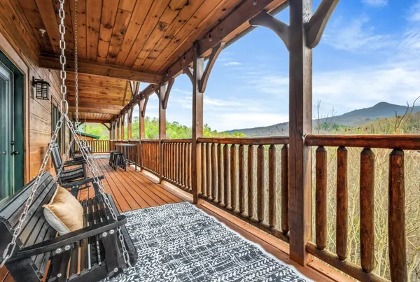 A porch swing hanging on chains at the end of a covered deck, the valley beyond the rail.