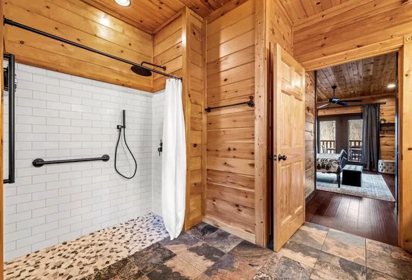 A walk in shower, white tile with a pebble floor.