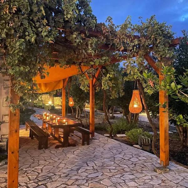 The long table at Armonia laid for dinner at dusk, lanterns hung from the vine pergola above it.