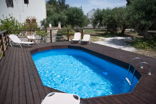 The pool at Armonia, set into a timber deck with loungers around it and olive trees behind.