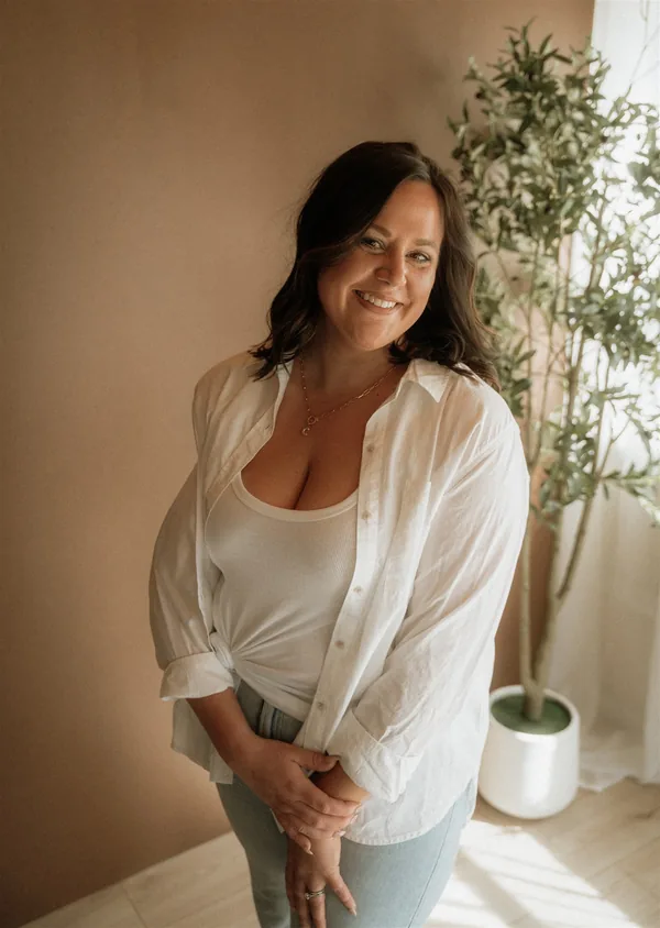 Cydnie Jocelyn, standing, hands together, in a white shirt against a warm wall.
